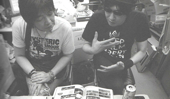 Minoru Ikeda, owner and operator of Mikado arcades in the Tokyo area, and author Gichi Otsuka sitting together at a table, drinking, and discussing arcade game history while looking at old magazines.