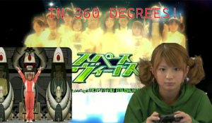 The background is Morning Musume dressed in their futuristic Space Venus costumes, and in front of it is the Space Venus logo along with a picture of Mari Yaguchi wearing a green hoodie and holding a PlayStation 2 controller. To her left is an image of her character in Space Venus emerging from what appears to be some sort of hibernation pod, enthusiastically.